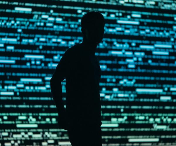 Surveillance, illustrated by the silhouette of a man in front of a data wall