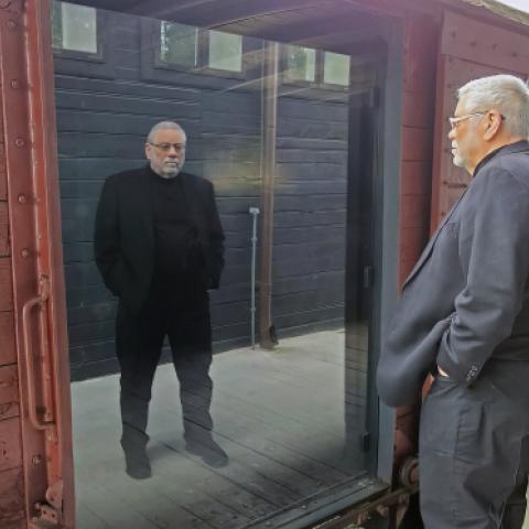 Edwin at the train station in Łódź, grey suit, looking at a boxcar exhibit